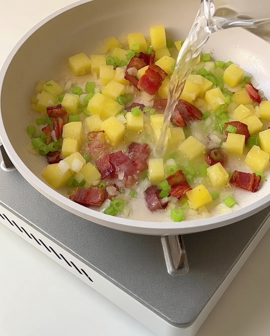 Caldo claro de almejas vertiéndose en una sartén con la mezcla de verduras salteadas y tocino.