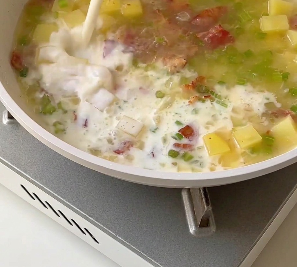 Una base cremosa de sopa de almejas mezclándose con leche, crema y carne de almeja en una sartén.
