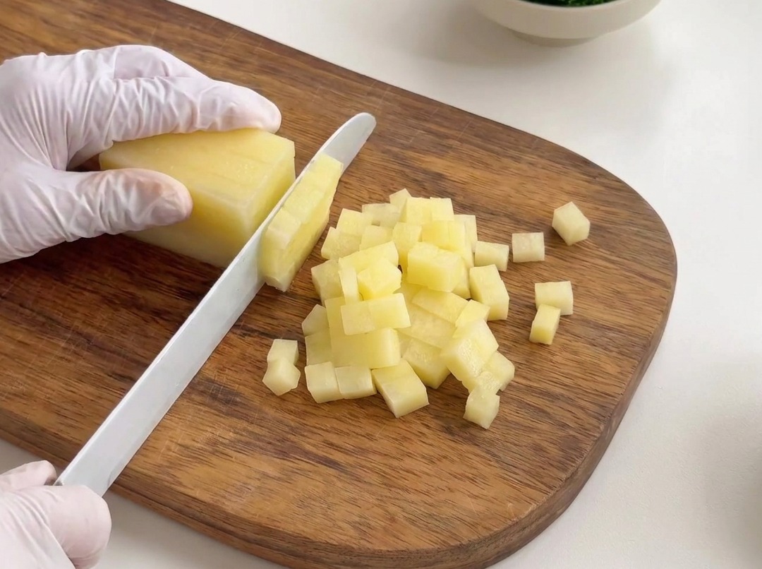Patatas peladas cortadas en cubos pequeños y uniformes sobre una tabla de madera.