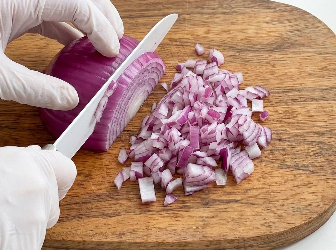 Cebolla morada siendo picada finamente sobre una tabla de madera.