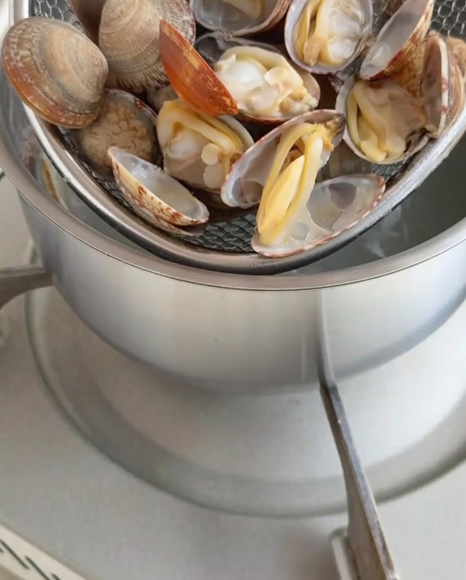 Carne de almeja cocida siendo extraída de sus conchas.