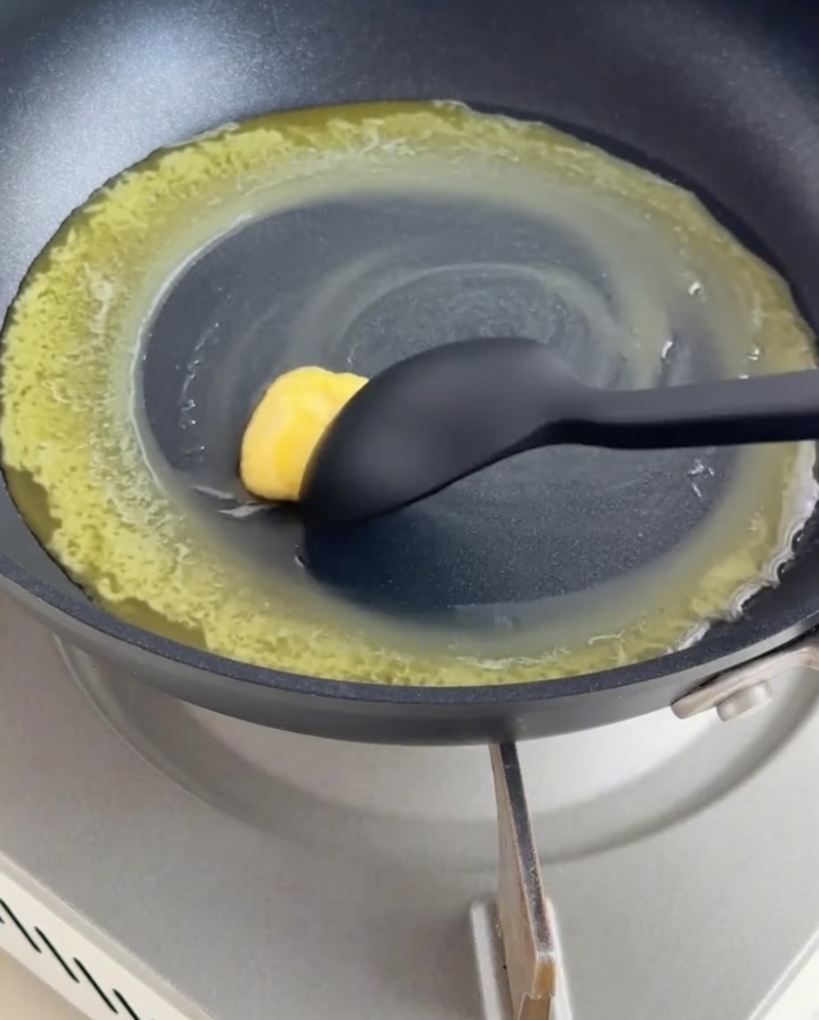 Sartén antiadherente con mantequilla derretida y harina siendo mezcladas.