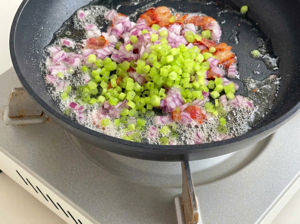 Patatas, apio y cebolla morada siendo salteados con el tocino y su grasa.
