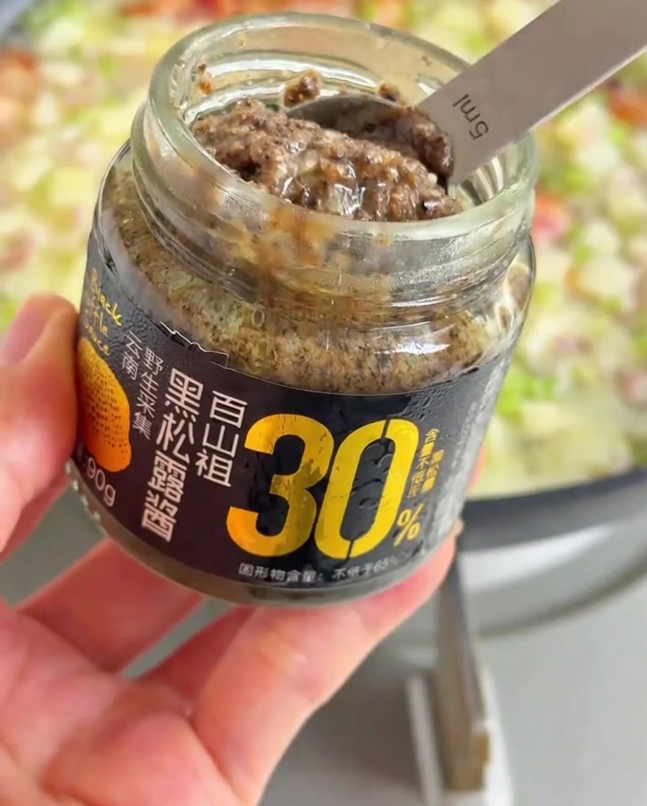 Una cucharada de pasta de trufa negra siendo añadida a la sartén burbujeante.