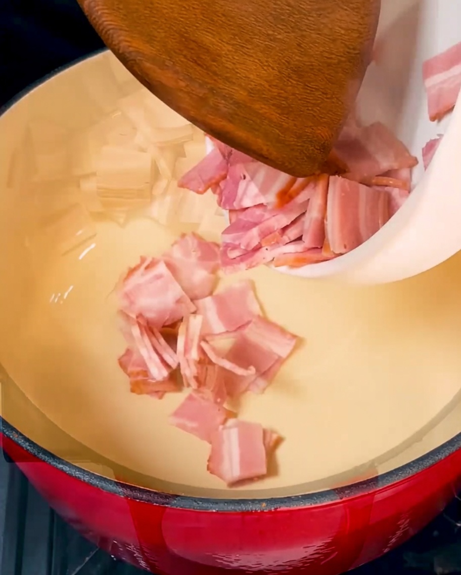 Trozos de tocino crujientes dorándose en una olla de hierro fundido roja.