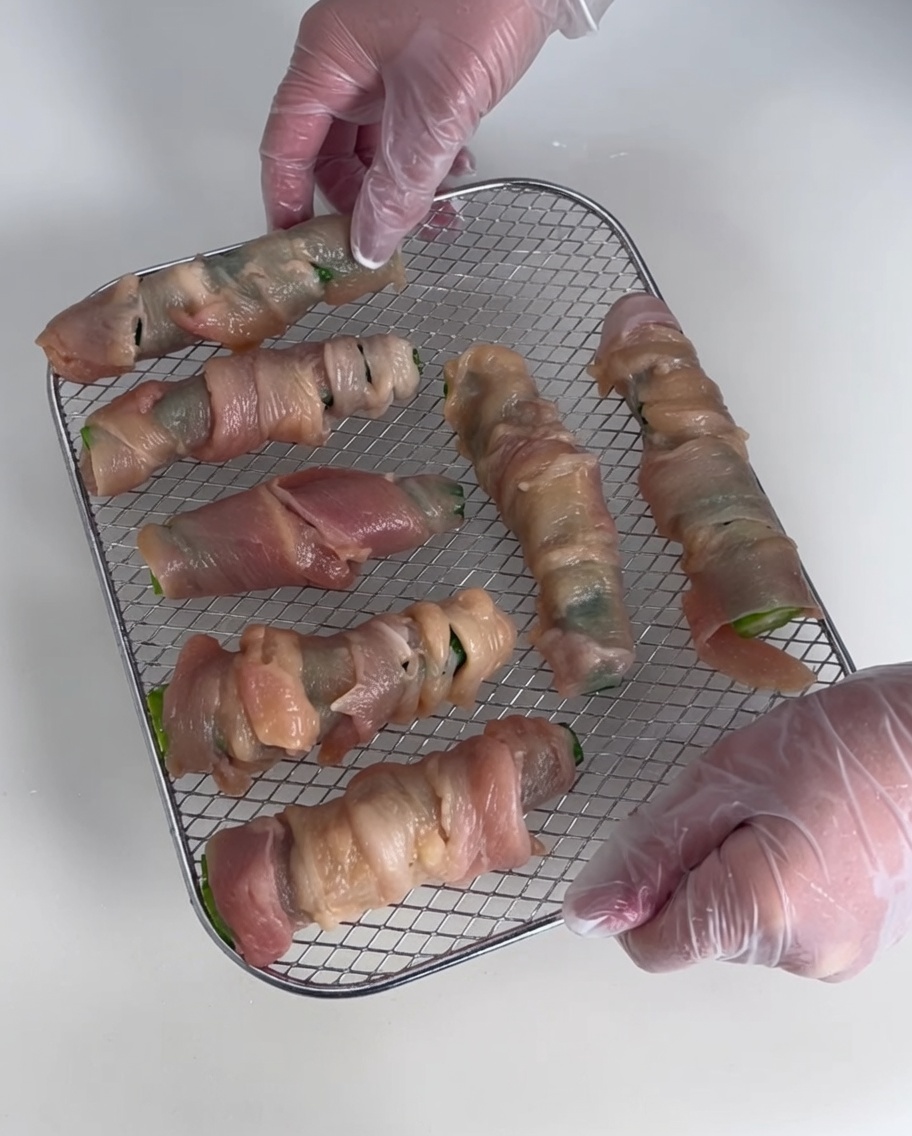 Varios rollitos de pollo y okra dispuestos sobre una rejilla de secado metálica.