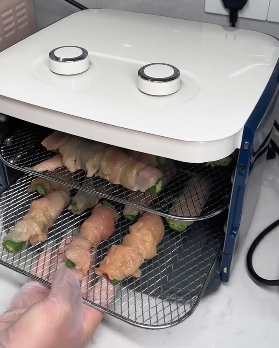 Rejillas de secado metálicas con los rollitos de pollo siendo introducidas en un deshidratador de alimentos.
