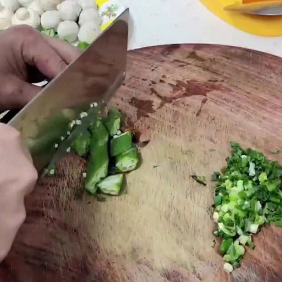 Segmentos de okra verde fresca siendo cortados sobre una tabla de madera.