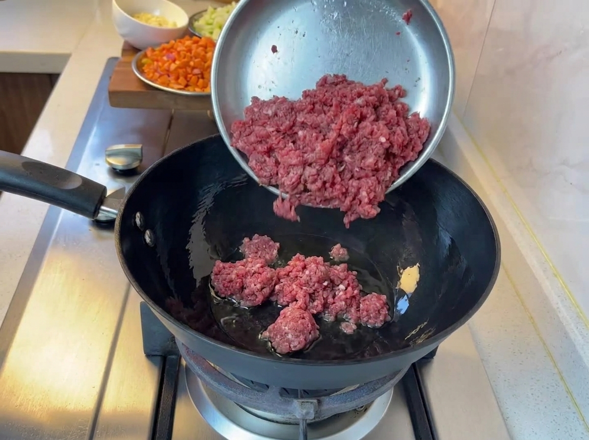Carne picada cocinándose en una sartén negra sobre una estufa de gas.