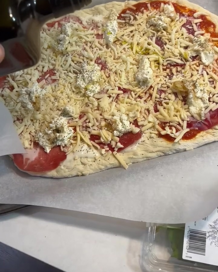 Un ligero chorro de aceite de oliva siendo aplicado sobre la pizza montada.