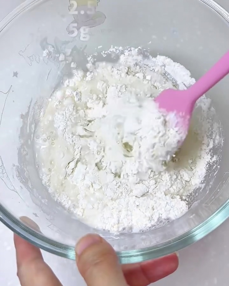 Ingredientes para la masa de pizza siendo mezclados en un bol grande de cristal con una espátula de silicona.