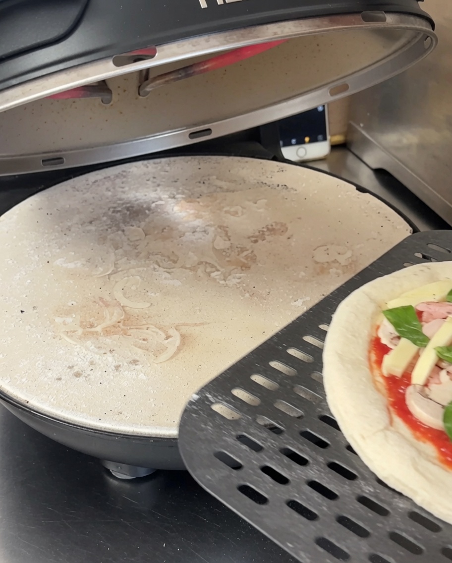 Masa de pizza aplanada sobre una piedra negra perforada dentro de un horno.
