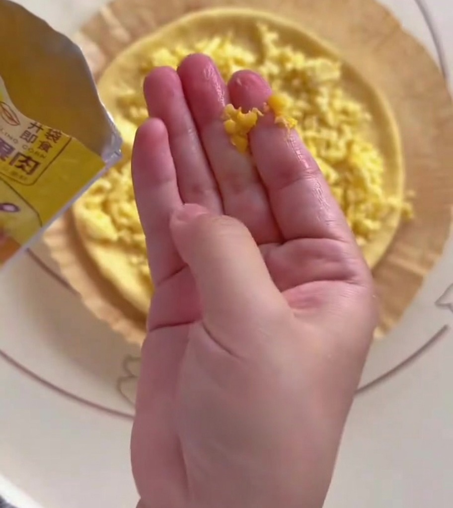 Mano esparciendo granos de maíz amarillo sobre la mitad de la masa de pizza.