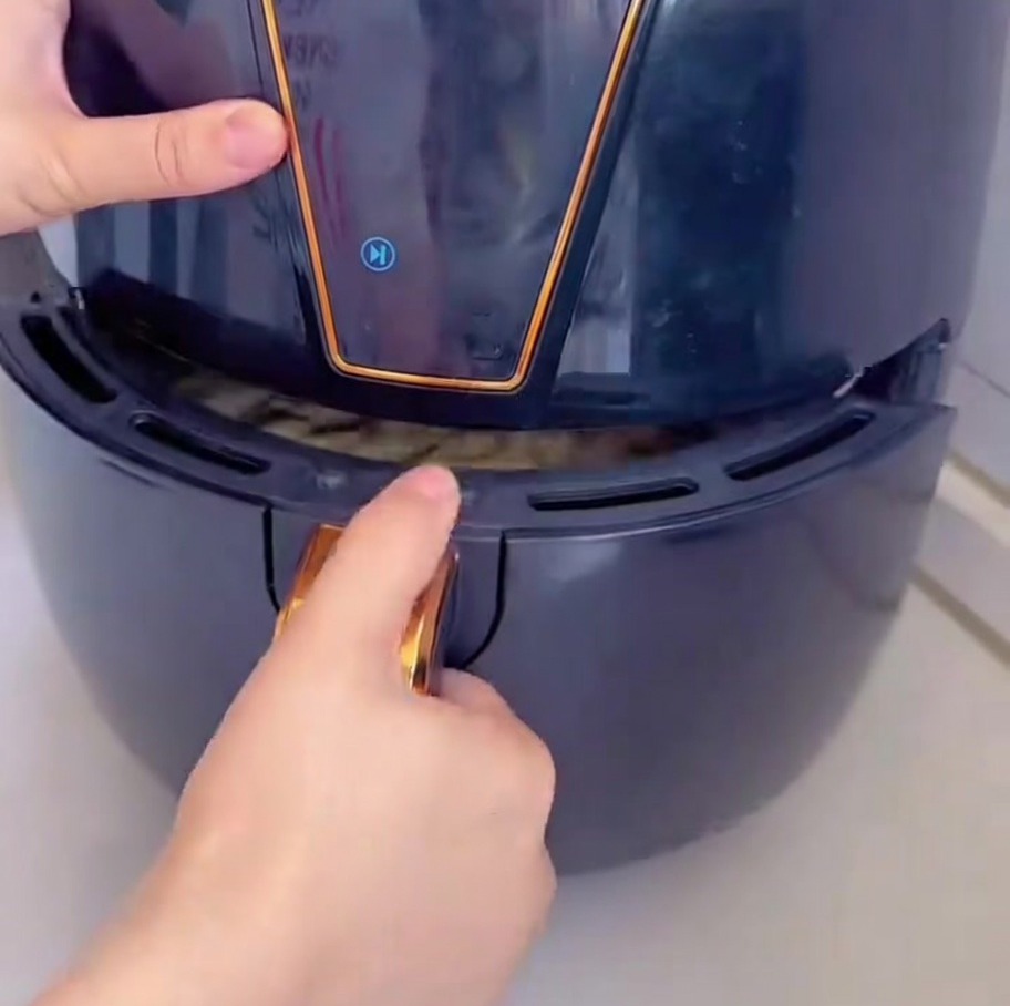 Vista de la mano deslizando el cajón de una air fryer negra con la pizza dentro.