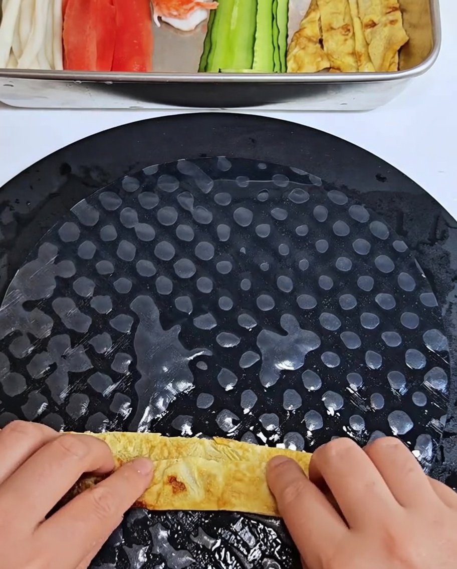 Tiras de tortilla de huevo siendo envueltas dentro de una lámina de papel de arroz suavizado.