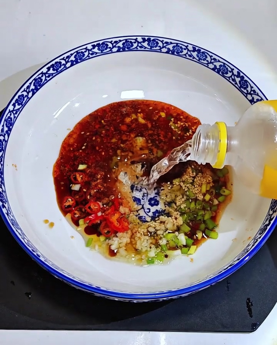 Agua clara siendo vertida de una botella en un tazón con la mezcla de salsa aromática.