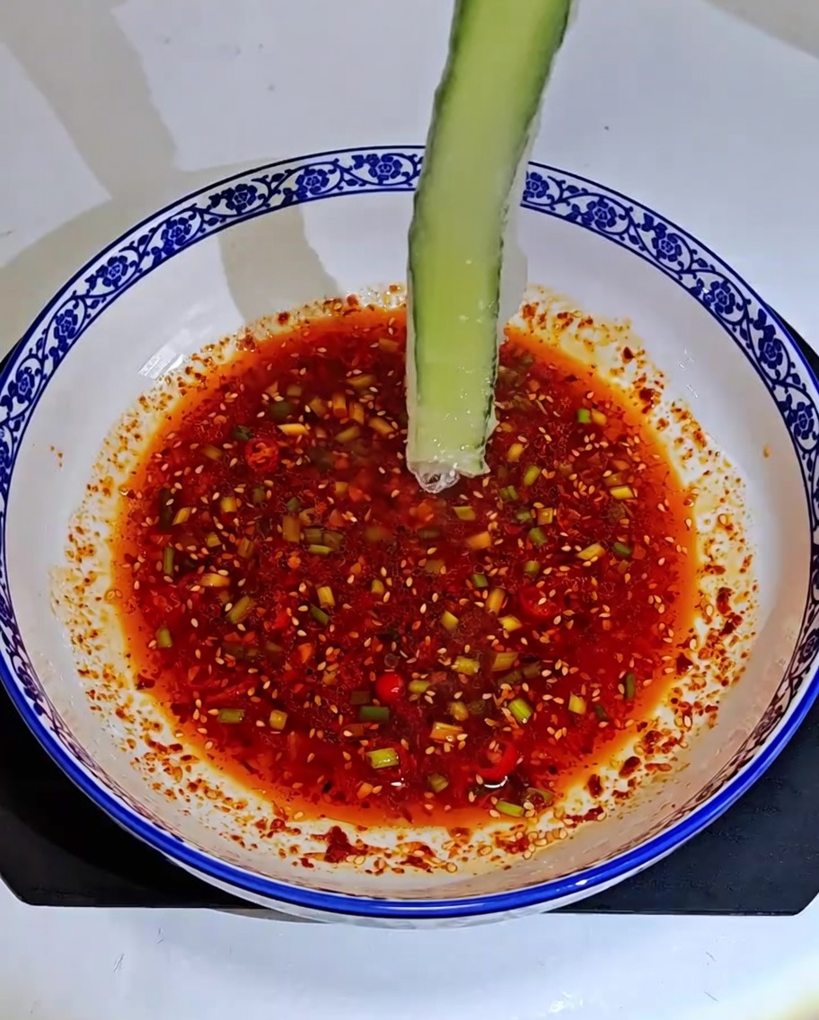 Rollitos de pepino y surimi siendo colocados dentro de una salsa para mojar en un tazón estampado.