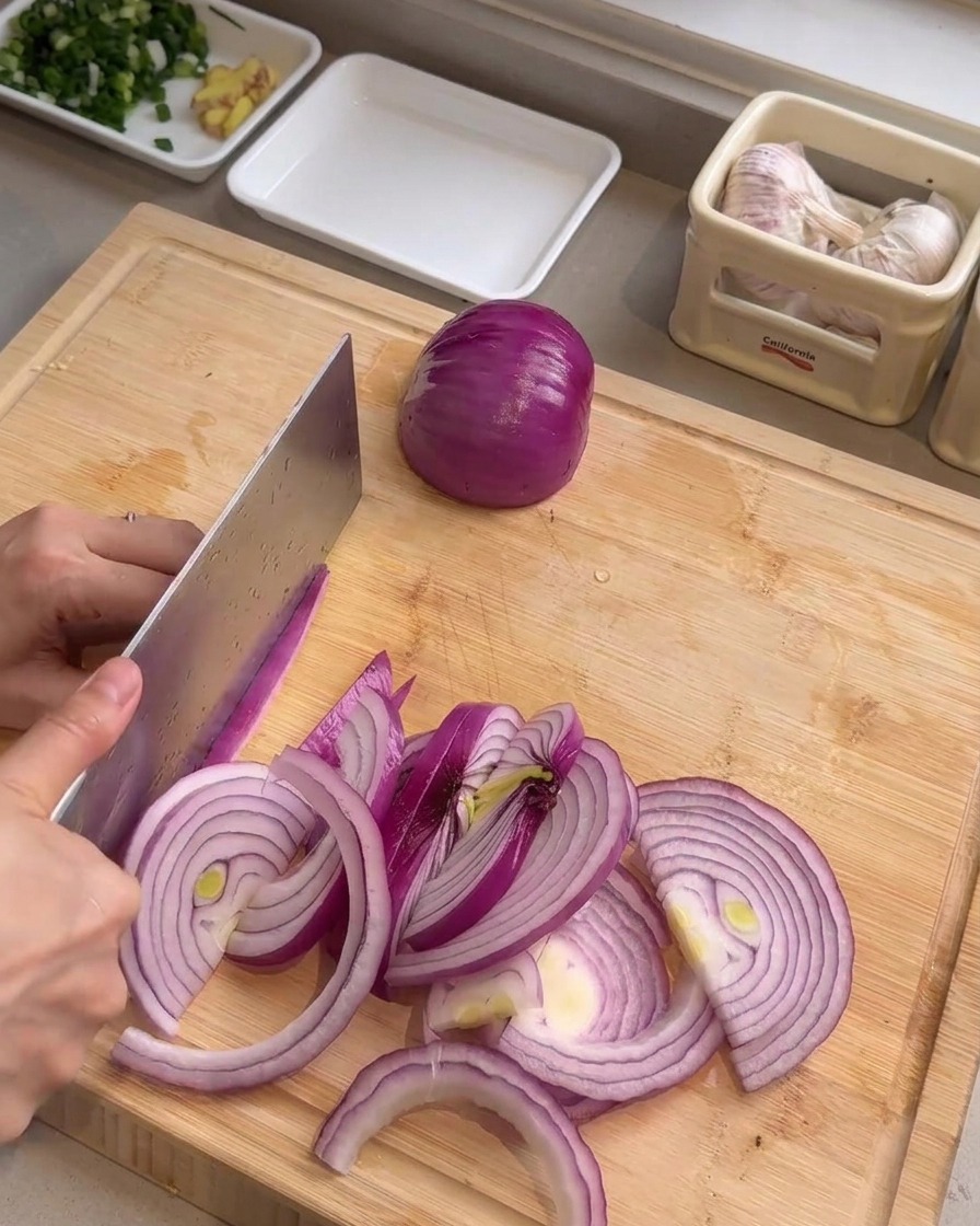Un cuchillo picando un cebollín verde en rodajas finas y circulares sobre una tabla de madera.
