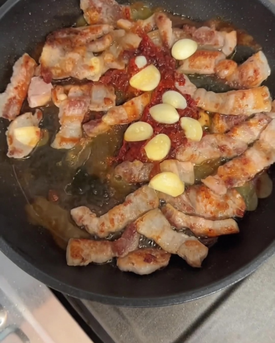 Panceta y ajo salteándose con la salsa en la sartén.