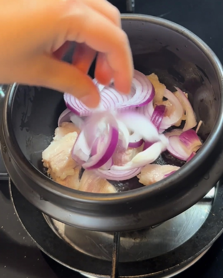 Rodajas de cebolla roja añadidas a la olla con la carne dorada.