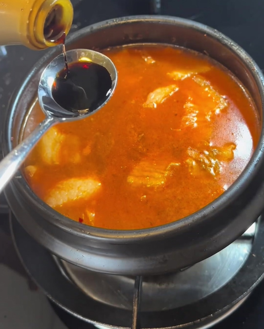 Una cucharada de salsa de soja siendo añadida al estofado hirviendo.