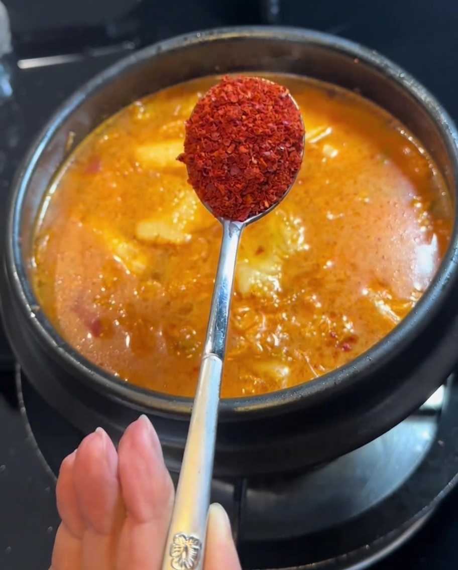 Polvo de chile siendo añadido al estofado con una cuchara.