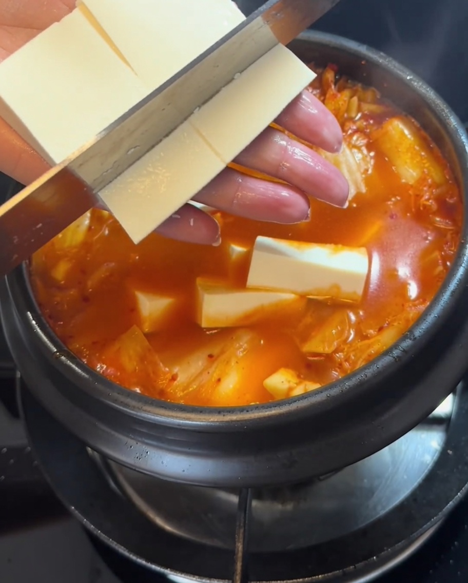 Rodajas de tofu firme siendo colocadas cuidadosamente en el estofado rojo burbujeante.