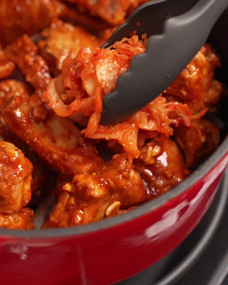 Una gran porción de kimchi sazonado colocándose sobre las costillas en la olla.