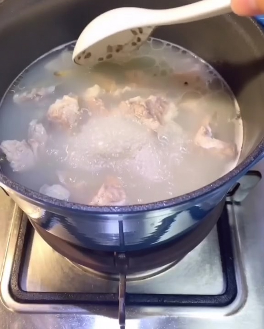 Costillas de cerdo cociéndose en una olla con agua en los fogones, empezando a formar un caldo claro.