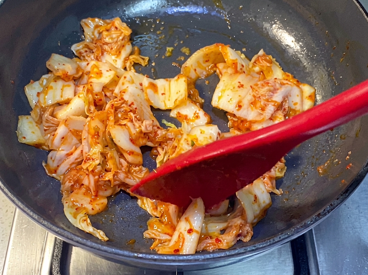Kimchi siendo salteado en una sartén con una espátula de silicona roja.