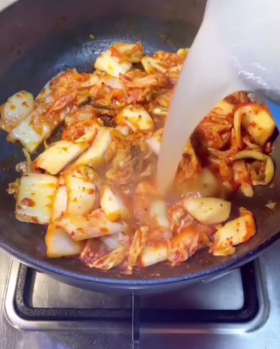 Caldo de costillas de cerdo siendo vertido en una olla que contiene kimchi salteado.