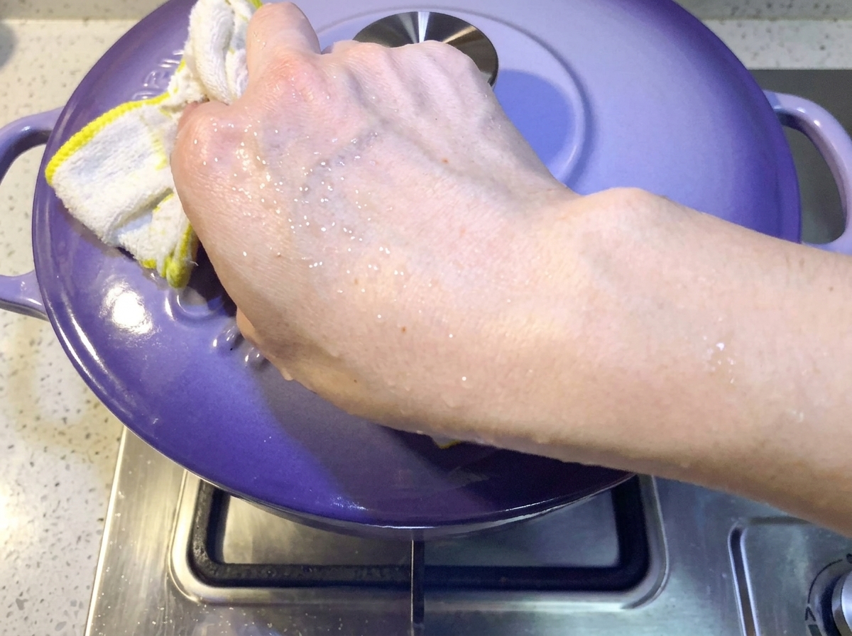 Mano colocando una tapa morada sobre la olla para cubrir el estofado de cerdo y kimchi.