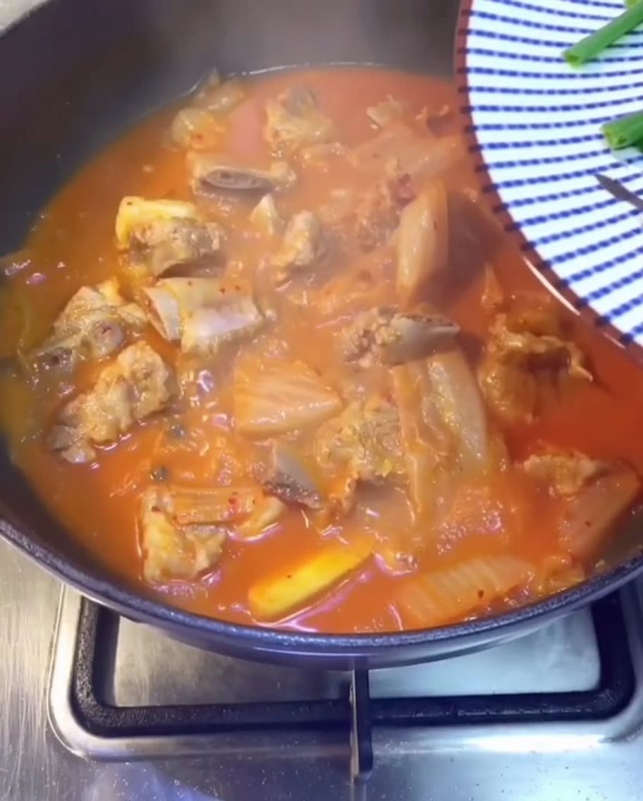 Un primer plano de cebolleta fresca, cilantro y chiles verdes en rodajas espolvoreados sobre el burbujeante estofado rojo de cerdo y kimchi.