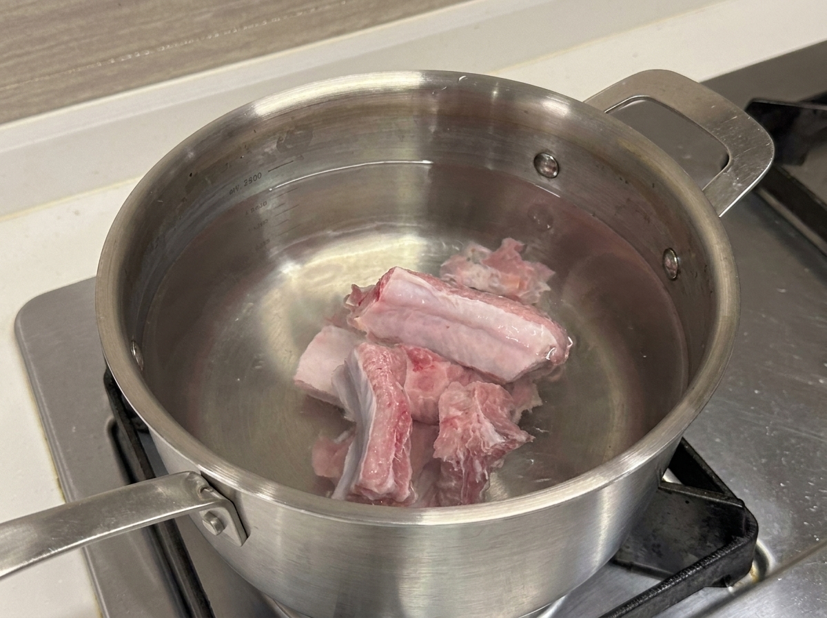 Costillas de cerdo crudas en una olla de acero inoxidable con agua fría.