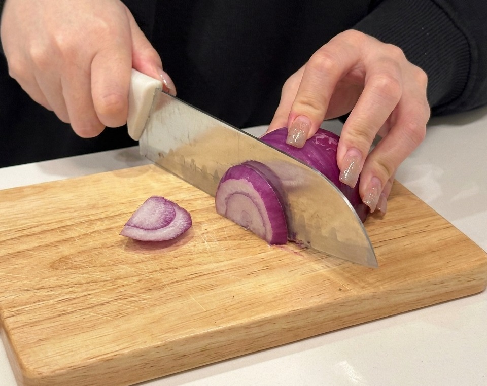 Manos cortando una cebolla morada sobre una tabla de madera.