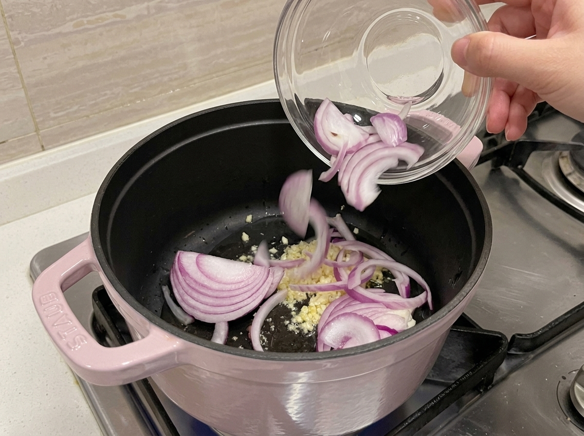 Ajo picado y cebolla morada sofriéndose en una olla con aceite.