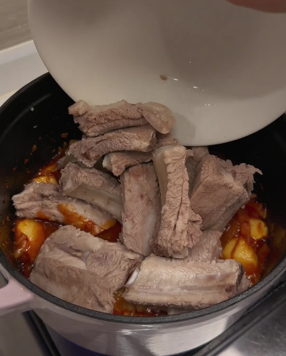 Costillas escaldadas siendo añadidas a la base de kimchi sazonada.