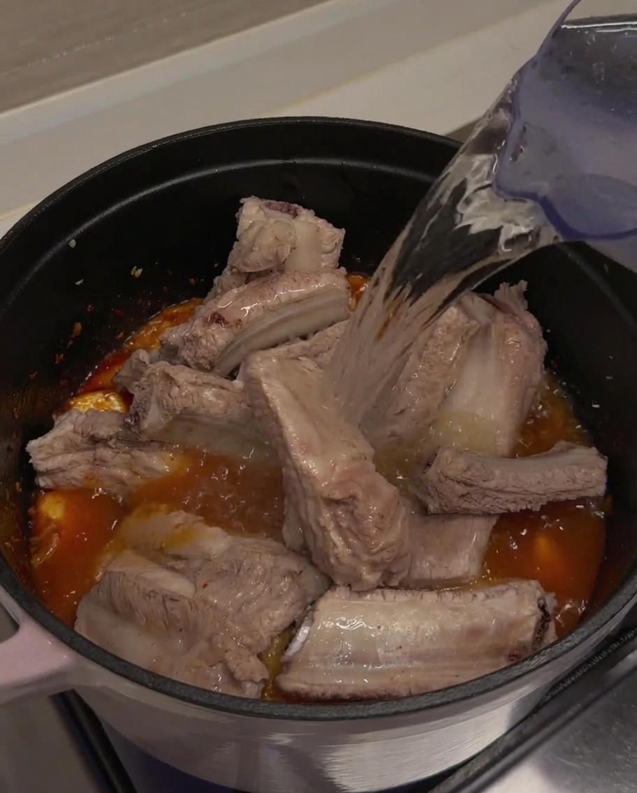 Agua siendo vertida en la olla hasta cubrir las costillas y el kimchi.