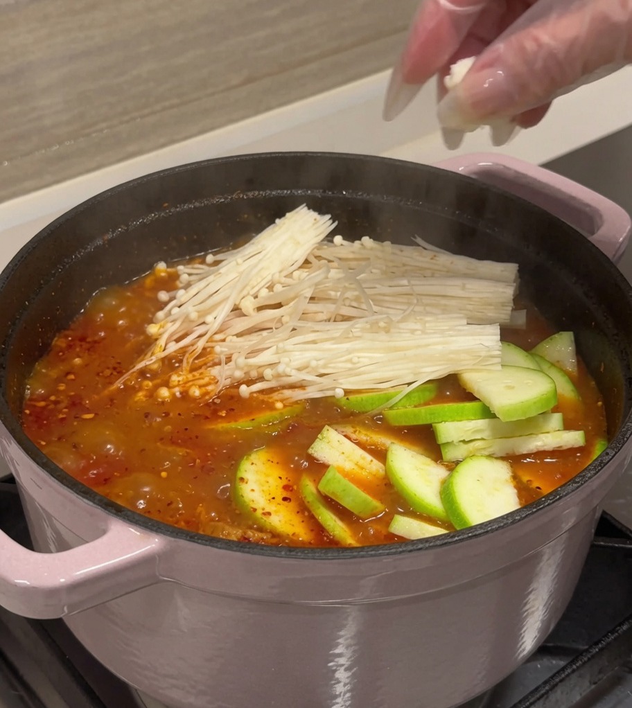 Calabacín, tofu y champiñones siendo añadidos al caldo hirviendo.
