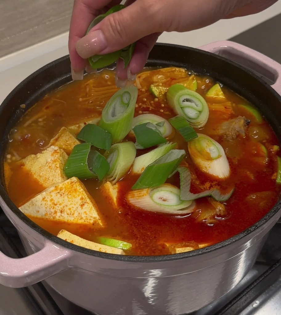 Cebolleta y chiles siendo esparcidos sobre la sopa terminada.