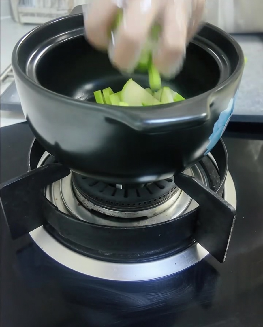 Calabaza verde y cebolla blanca cortadas en cubos, colocadas dentro de una olla de cerámica negra.