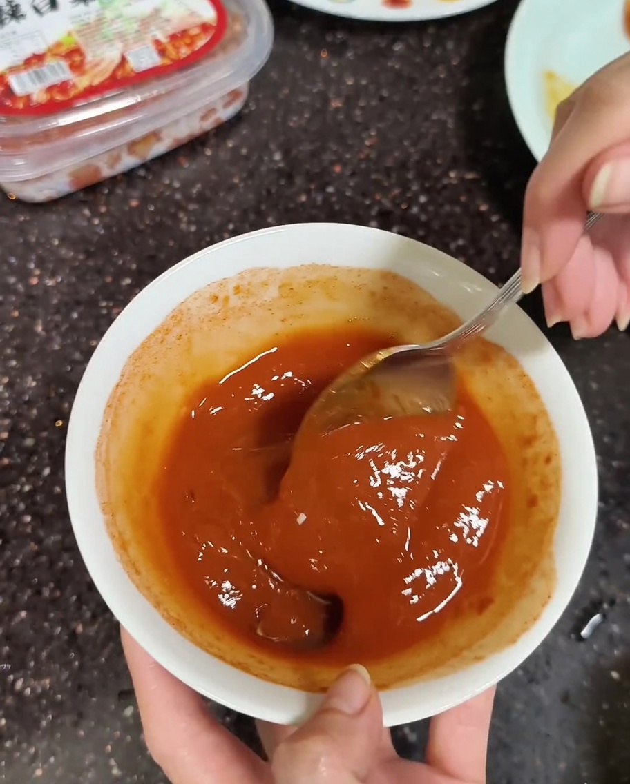 Primer plano de una cuchara mezclando pastas de soja y chile coreanas con un poco de agua hasta que quede suave.