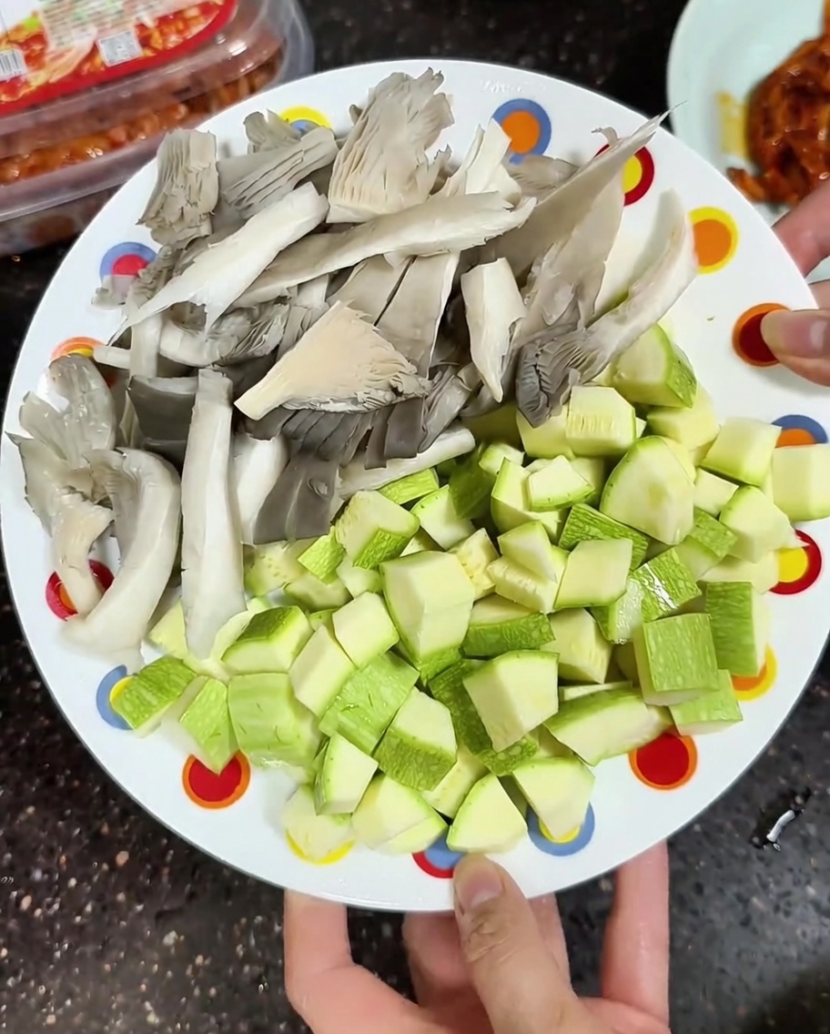 Un plato con setas de ostra grises frescas en rodajas y calabacín verde claro cortado en dados listo para cocinar.