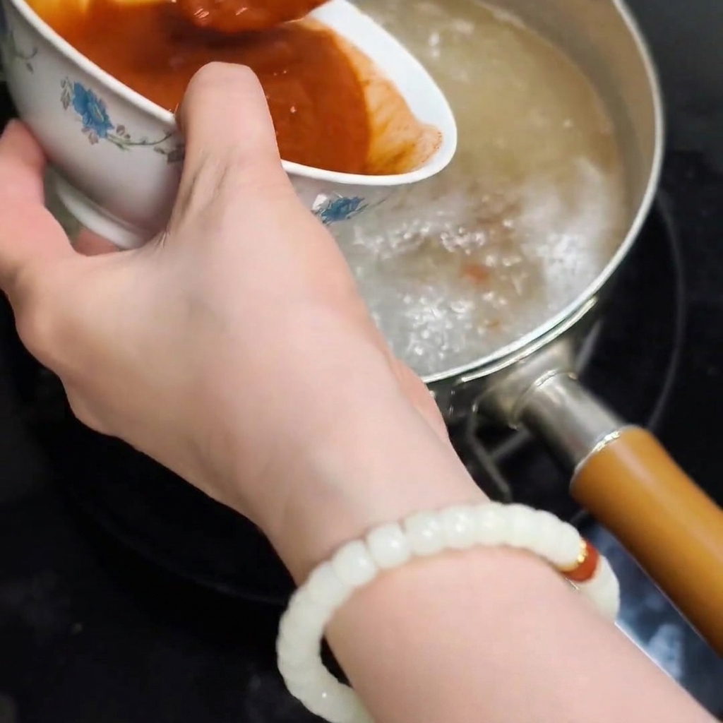 La suave mezcla roja de pasta disuelta vertiéndose desde un tazón al agua hirviendo en la olla.
