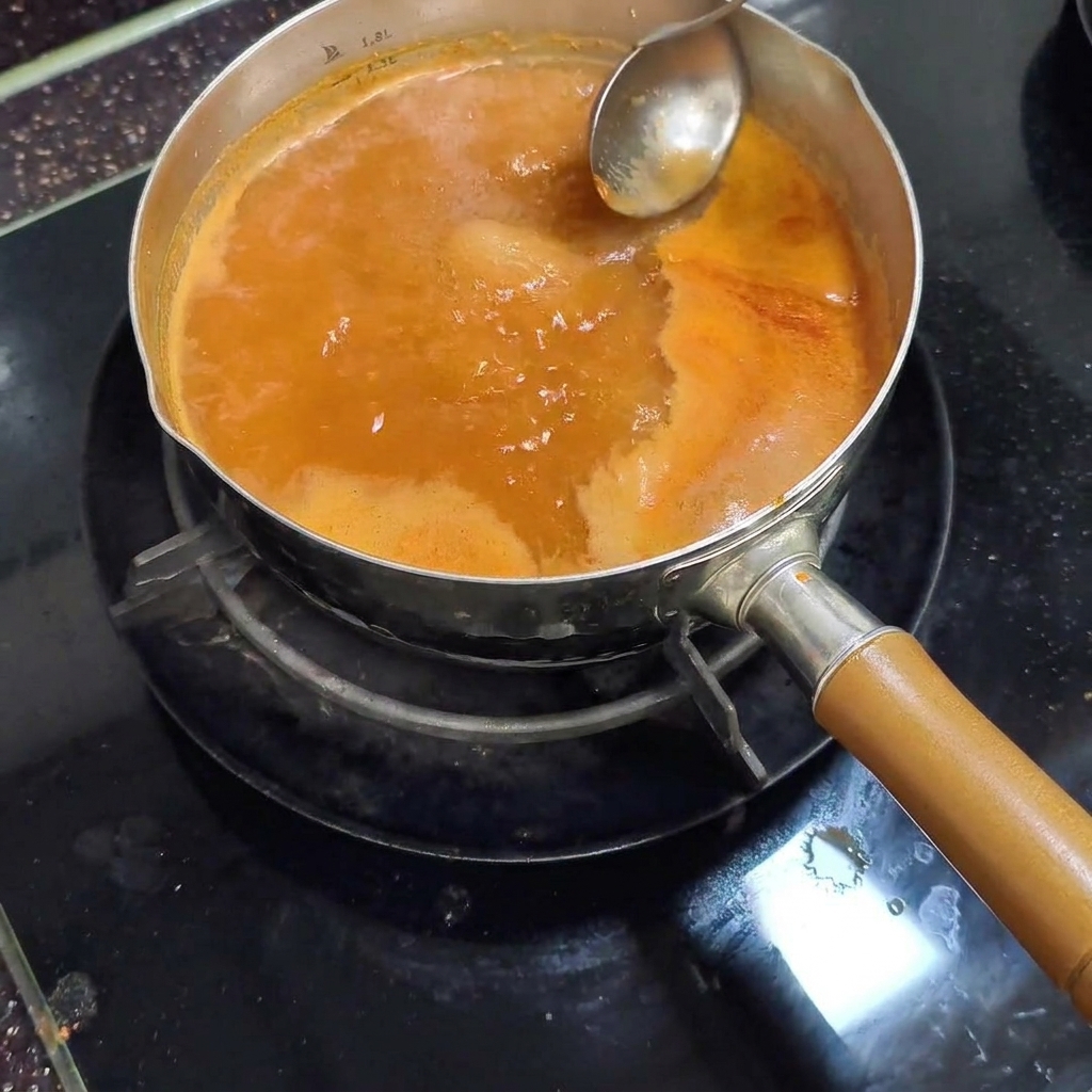 Un cazo de metal retirando espuma de color claro de la superficie del caldo rojo a fuego lento.