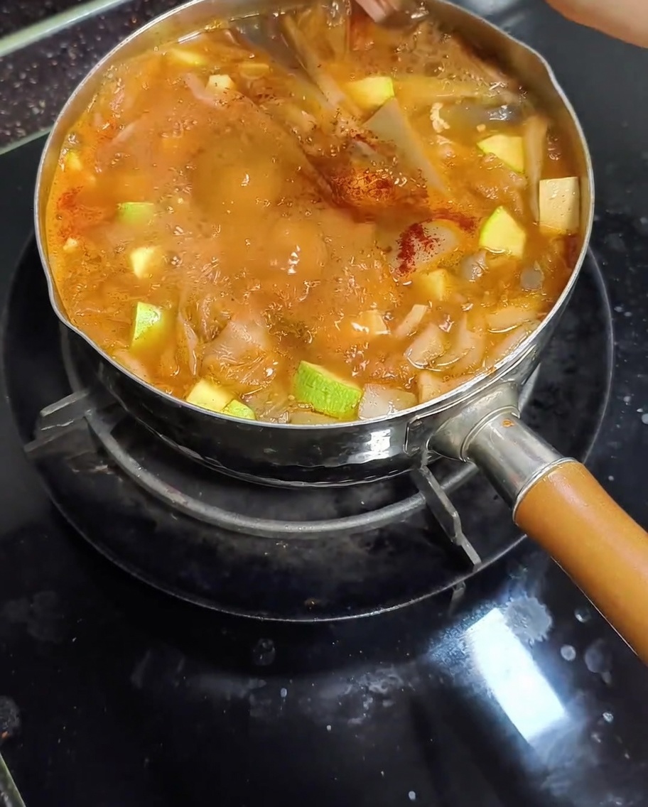 Pimentón dulce rojo espolvoreado en una olla de estofado de pasta de soja coreano hirviendo que contiene calabacín y setas.