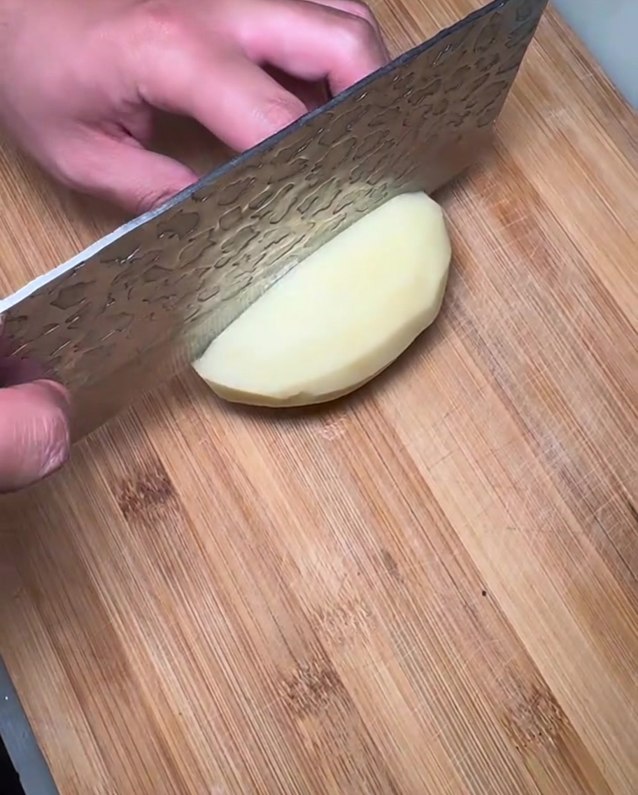 Rodajas de patata cruda dispuestas sobre una tabla de cortar de madera, listas para el estofado.
