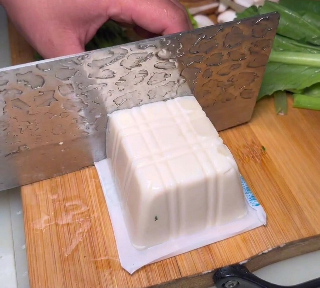 Bloques de tofu sedoso cortados en trozos gruesos sobre una tabla de cortar.