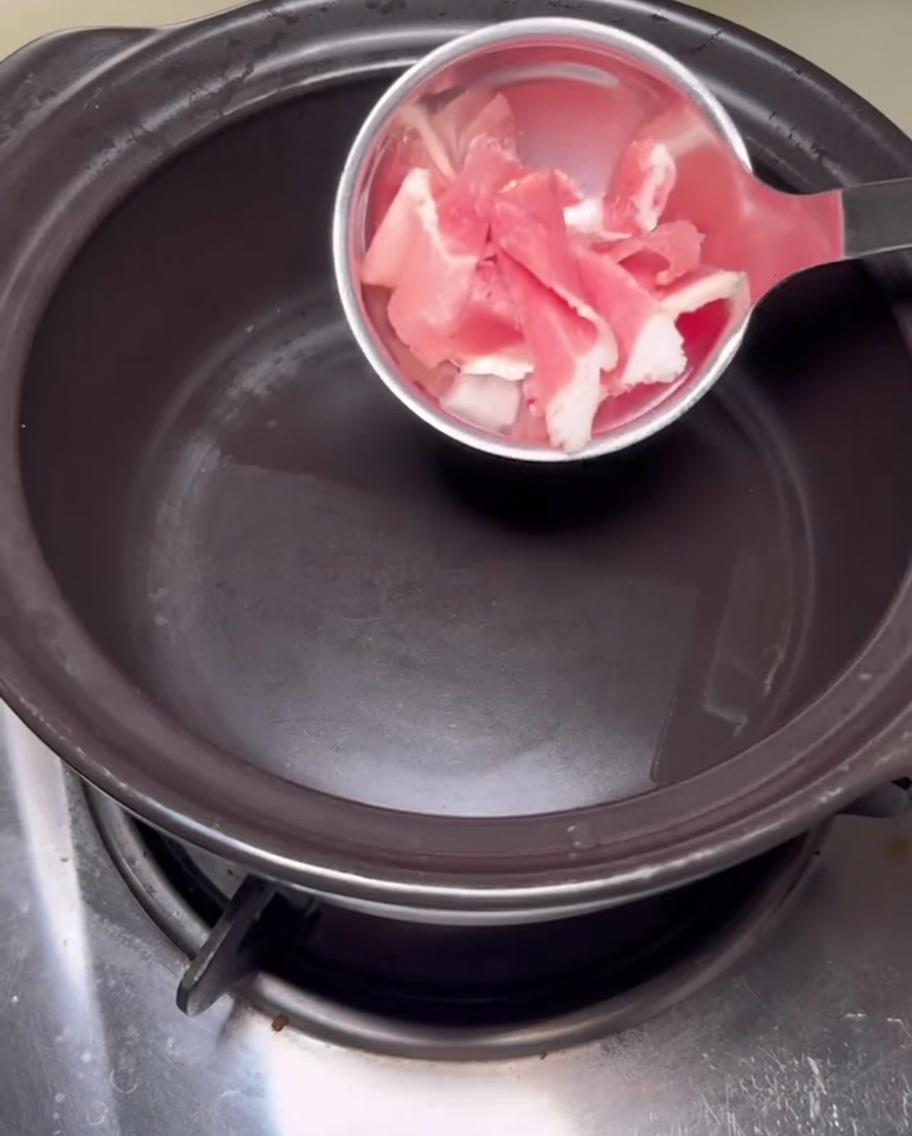 Rodajas de panceta de cerdo cruda friéndose en una olla de piedra negra caliente.
