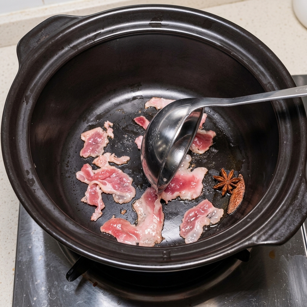 Rodajas de panceta de cerdo friéndose en una olla de piedra oscura, moviéndose con un cucharón.
